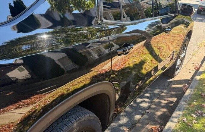 Black SUV paint reflecting the sky and trees
